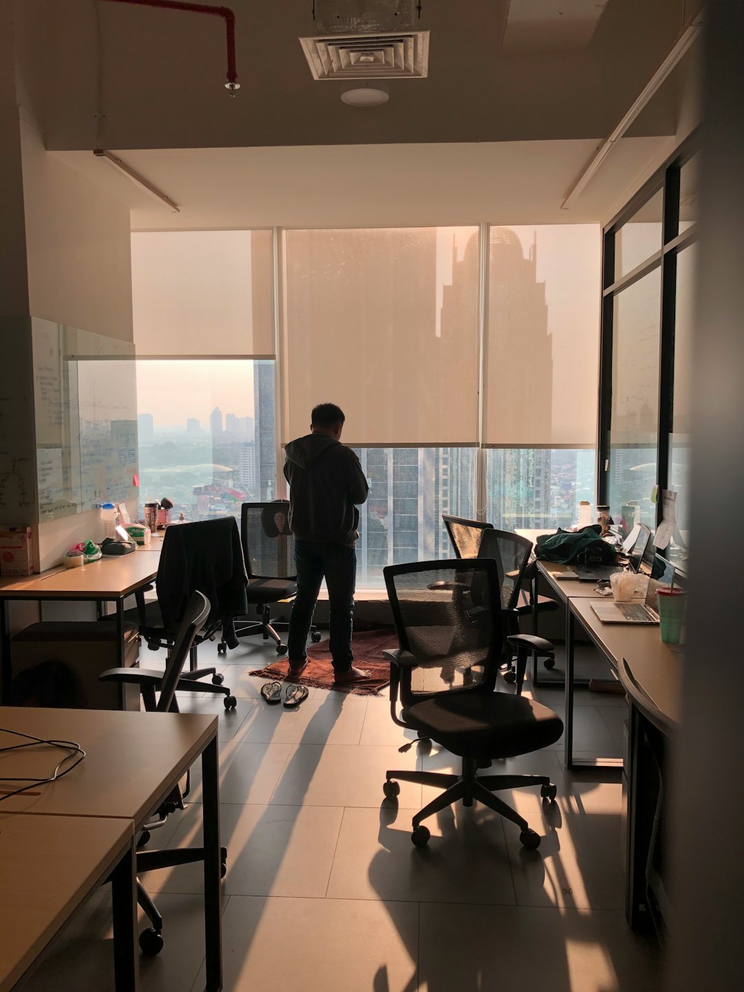 Person looks out office window at city skyline at sunset.